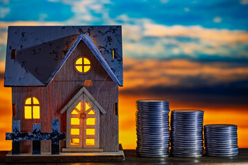 Small toy house model and stack of coins on table, nature background at night, closeup. Concept of land transfer taxation and Investment income tax from asset