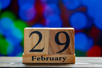 Wooden calendar with the date February 29 on the table against the backdrop of multicolored glowing lights, closeup