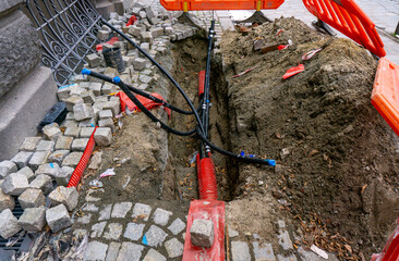 Street excavation with red safety barriers, groundworks for underground infrastructure repair, urban network modernization during road maintenance in public city area