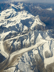 Flying over the European Alps during fall season. Aerial view from the airplane window. Fresh snow on the peaks. View of the glaciers