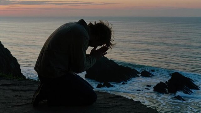 Man in silhouette finds peace praying on a cliff at sunset overlooking the ocean, seeking hope, faith, and spirituality in nature's beauty