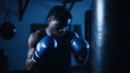 African american man boxer punching training bag at night. Dark gym with boxing accessories for sport martial arts footage. - Powered by Adobe