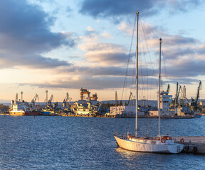 Sailboat at Sunset in Yacht Harbor With Industrial Dockyards and Cranes in Background Alight, Varna city, Bulgaria