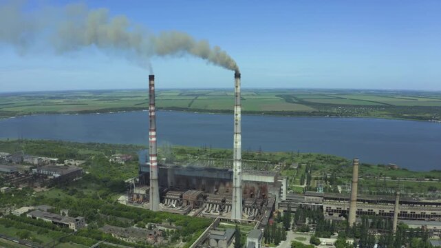 Aerial view of coal-fired thermal power plant with smoke emissions near a river and green fields