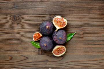 Purple ripe figs fruit and slices with green leaves top view on a wooden background