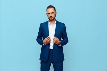 A professional man in a sharp blue suit stands against a solid blue backdrop, projecting confidence and calm as he adjusts his jacket with deliberate poise. © SHOTPRIME STUDIO