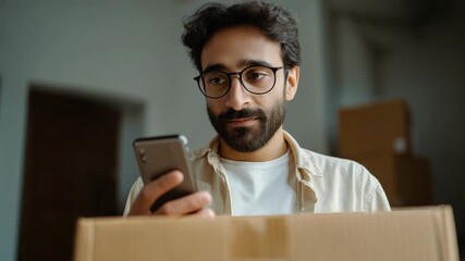 Man smiles at his phone while holding a cardboard box, enjoying a moment of surprise and joy - Powered by Adobe