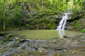 Ton Rak Sai Waterfall (Long exposure) cascading into the emerald natural pool, surrounded by mossy rocks and lush jungle in Namtok Sam Lan National Park, Saraburi, Thailand.