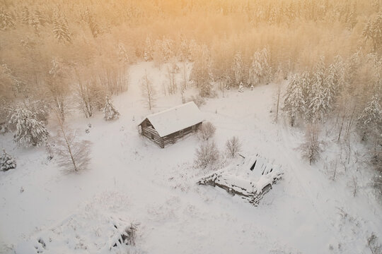 Aerial view of an abandoned village in the forest with destroyed houses against the backdrop of snow and winter landscape. Warm sunset color