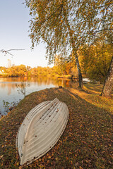 overturned boat is lying on the shore of a pond in autumn