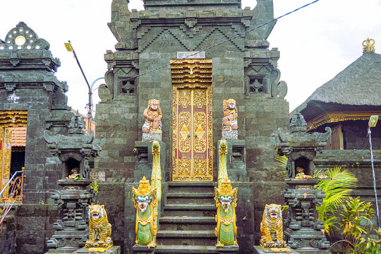 Ornate entrance to a traditional Balinese Hindu temple with intricate stone carvings, golden doors, and guardian statues