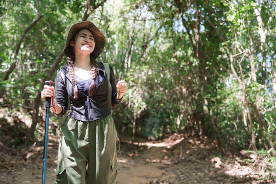 Young woman enjoying sunny forest hike with trekking pole