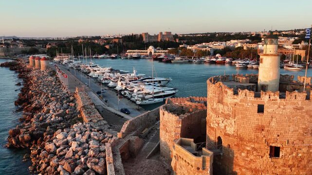 Mandraki harbour and fort of saint nicholas in rhodes greece at sunset showing many yachts and the ancient walls