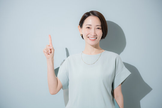 綺麗なミントグリーン背景のビジネス女性イメージ　上半身正面で指差しポイントポーズ