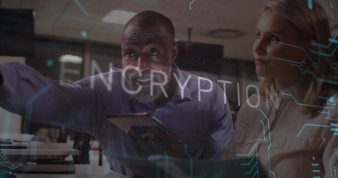 Senior IT specialist holding tablet gesturing toward monitor, keyboard in office encryption overlay - Powered by Adobe