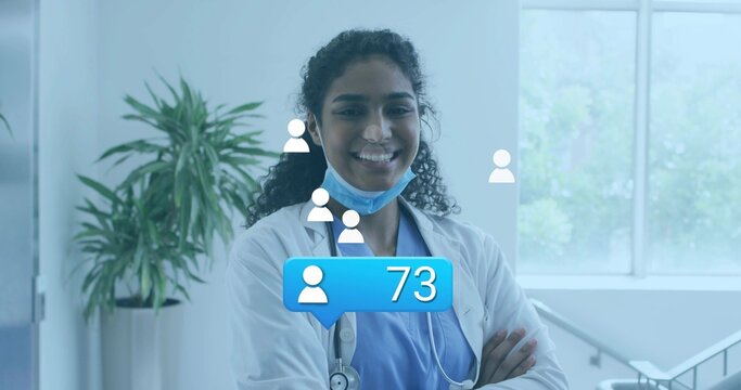 Standing doctor wearing lab coat and scrubs with stethoscope, mask, digital icons in medical office - Powered by Adobe