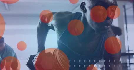 African American man wearing tank top performing single arm dumbbell row in gym, with red circles