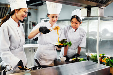 Team of professional chefs in a commercial kitchen plating noodles and greens, collaborating during...