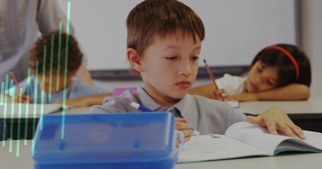 Writing boy focusing on workbook at classroom desk, with blue pencil case and supplies
