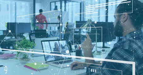 Gesturing bearded worker pointing at laptop showing remote call at office desk with smartphone