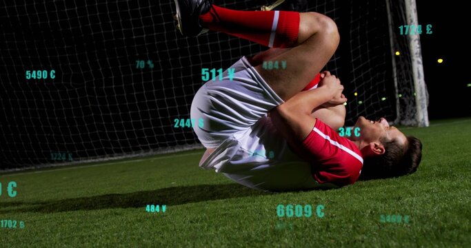 Lying player in red kit clutching knee on pitch at floodlit net, with floating currency overlays