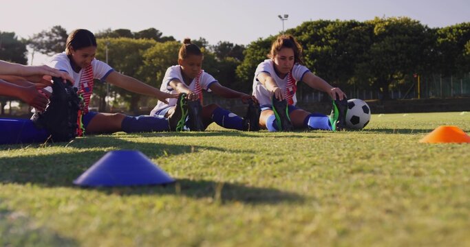Stretching three soccer players reaching toward toes on grass pitch, with cones and soccer ball