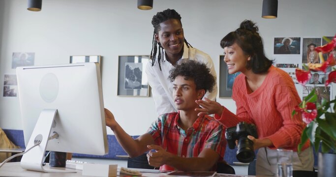 Pointing photographer in orange sweater discussing project on desktop in studio, with DSLR camera