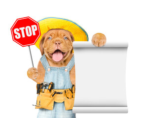 Happy mastiff puppy wearing summer hat and denim overalls with tool belt shows stop sign and empty list. Isolated on white background