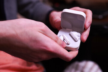 Hands holding a white wireless earbuds case with the lid open, displaying the earbuds inside. The image captures the modern design and portability of these audio devices.