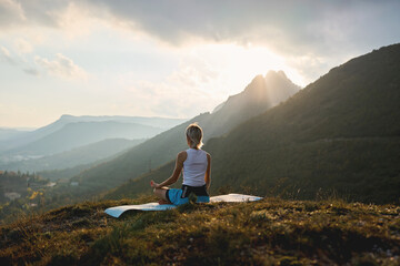Fototapeta premium Woman meditating on mountain at sunrise with sunlight rays