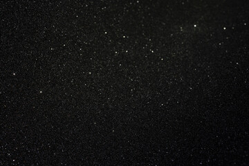 Black texture with golden inclusions and rare sparkles, abstract surface glowing subtly with scattered highlights across dark granular depth