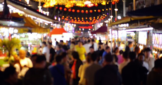 Slow motion defocused view of people crowd at night street market of Kuala Lumpur. Visitors walk along stalls of street food and snacks and affordable restaurants at famous food street at downtown