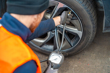 Worker checking tire pressure with gauge after seasonal wheel replacement. Final step of winter tire preparation in auto service in Czech Republic.