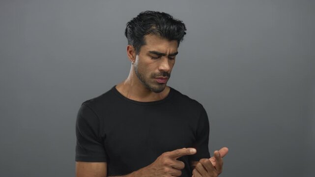 Man points finger to finger in grey studio under dramatic lighting with focused expression; contemplation.