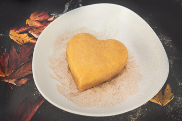 Heart-shaped shortcrust pastry on a floured dark surface, surrounded by autumn maple leaves — cozy seasonal baking and fall-inspired homemade cookie preparation moment.