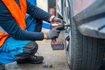 Mechanic using an impact wrench to remove lug nuts from a car wheel. Seasonal tire change and professional car service in preparation for winter.