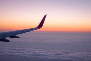 Obraz premium Aerial view from an airplane window with a plane's wing silhouetted against a vibrant sunset sky, above a sea of fluffy clouds, capturing the essence of travel and serene beauty.