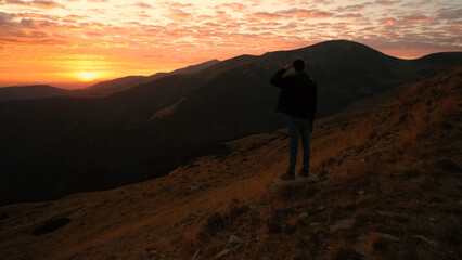 Man enjoying a sunset view while standing on a mountain slope during a calm evening in nature