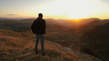 Fototapeta premium Man standing on a mountain ridge watching the sunset over the valley on a clear evening