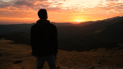 Man enjoying a breathtaking sunset view from a mountain peak, surrounded by vast landscapes and dramatic clouds, creating a peaceful moment in nature