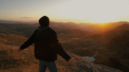 Man enjoying the sunset view on a mountain while standing with arms open, embracing nature s beauty after a long hike in the evening