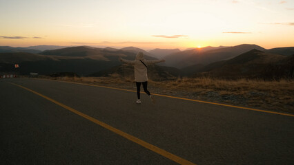 Woman enjoying a scenic sunset walk along the road in the mountains during golden hour, embracing nature and tranquility in a serene landscape