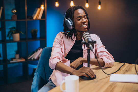 Young african american podcaster speaking into a microphone while recording a podcast episode in a home studio - Powered by Adobe