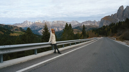 Woman enjoying a scenic mountain view while leaning against a guardrail along a winding road in a tranquil landscape