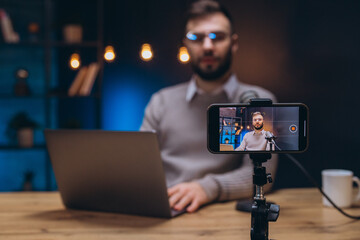 Professional podcaster working on smartphone, recording audio content in minimalist home studio with dedicated microphone setup