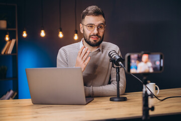 Young man recording a podcast using professional microphone and smartphone in a home studio with laptop