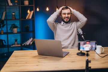 Happy podcaster streaming online from a modern home studio, using a smartphone and microphone to create engaging content