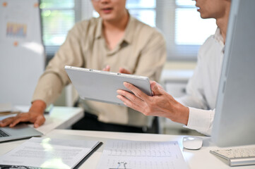 Fototapeta premium Close up of a businessman talking while looking at tablet of coworker at table in company's office.