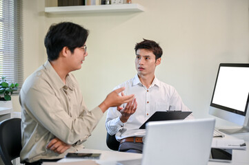 Asian businessman talking discussing with coworker as holding clipboard at table in company's office