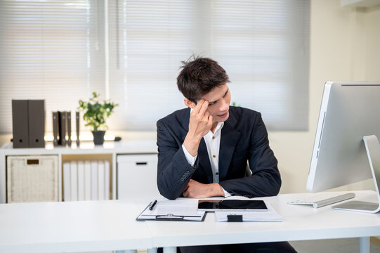 Confused asian businessman scratching head looking at computer on working table in company's office. - Powered by Adobe